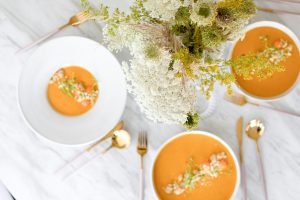 Schalen mit cremiger Suppe und frischen Kräutern, dekoriert mit einem Blumenarrangement auf einem Tisch.