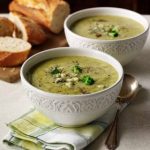 Zwei Schalen Brokkoli-Cremesuppe mit Brot und grünem Gemüse, serviert auf einem Tisch.