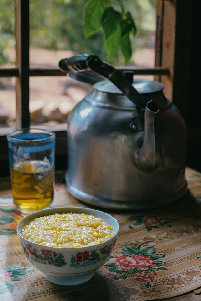 Eine Schüssel mit gelbem Blumenkohlsuppe steht neben einer Teekanne und einem Glas Tee auf einem Tisch.